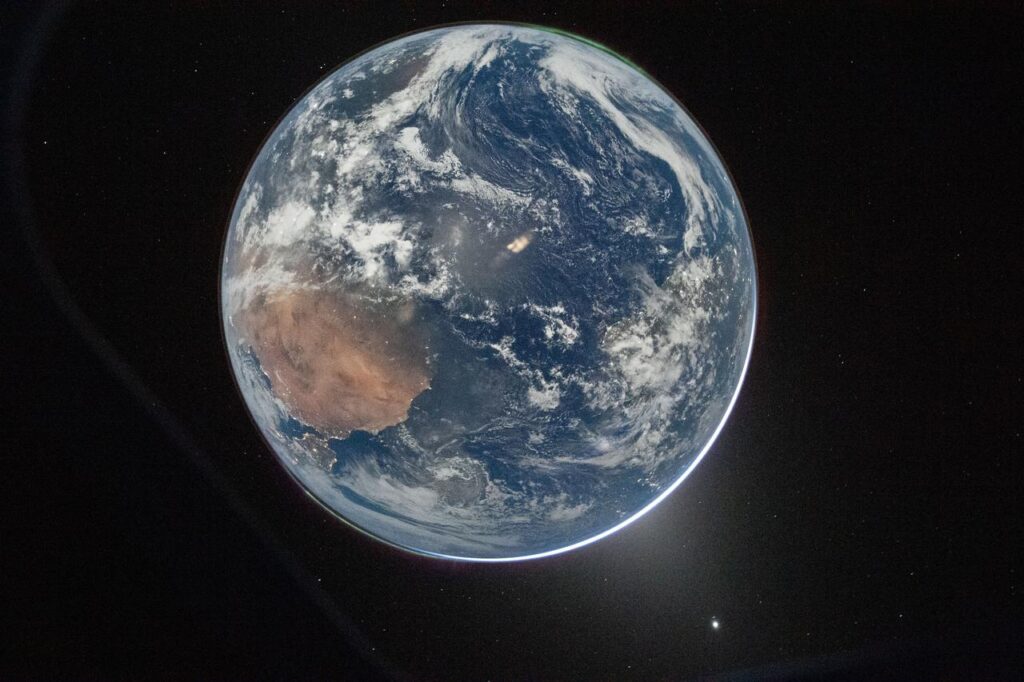 Earth From the Perspective of Artemis II NASA ID: art002e000192 art002e000192 (April 3, 2026) - This nighttime picture of Earth was taken on April 2, 2026, by an Artemis II crew member aiming a camera through a window of the Orion spacecraft. The image was captured after Orion completed its translunar injection burn, the critical maneuver that sent the spacecraft on its path toward the Moon and back. The visible hemisphere appears awash in sunlight, but it is actually lit by moonlight — sunlight reflected from the lunar surface. Along the upper left (south) and lower right (north) edges of Earth’s disk, green auroras glow against the dark sky, showing charged particles from the Sun interacting with gases in Earth’s atmosphere. Africa is visible on the left, while a translucent cone of light capped by a bright Venus extends into space from Earth’s lower right edge. This zodiacal light is caused by sunlight reflecting off interplanetary dust. A thin white crescent along the lower right edge of Earth marks the planet’s daytime atmosphere illuminated by the Sun, which lies on the opposite side of Earth from Orion’s perspective. City lights are also visible, especially along coastlines. Credits: NASA less Date Created:2026-04-03
